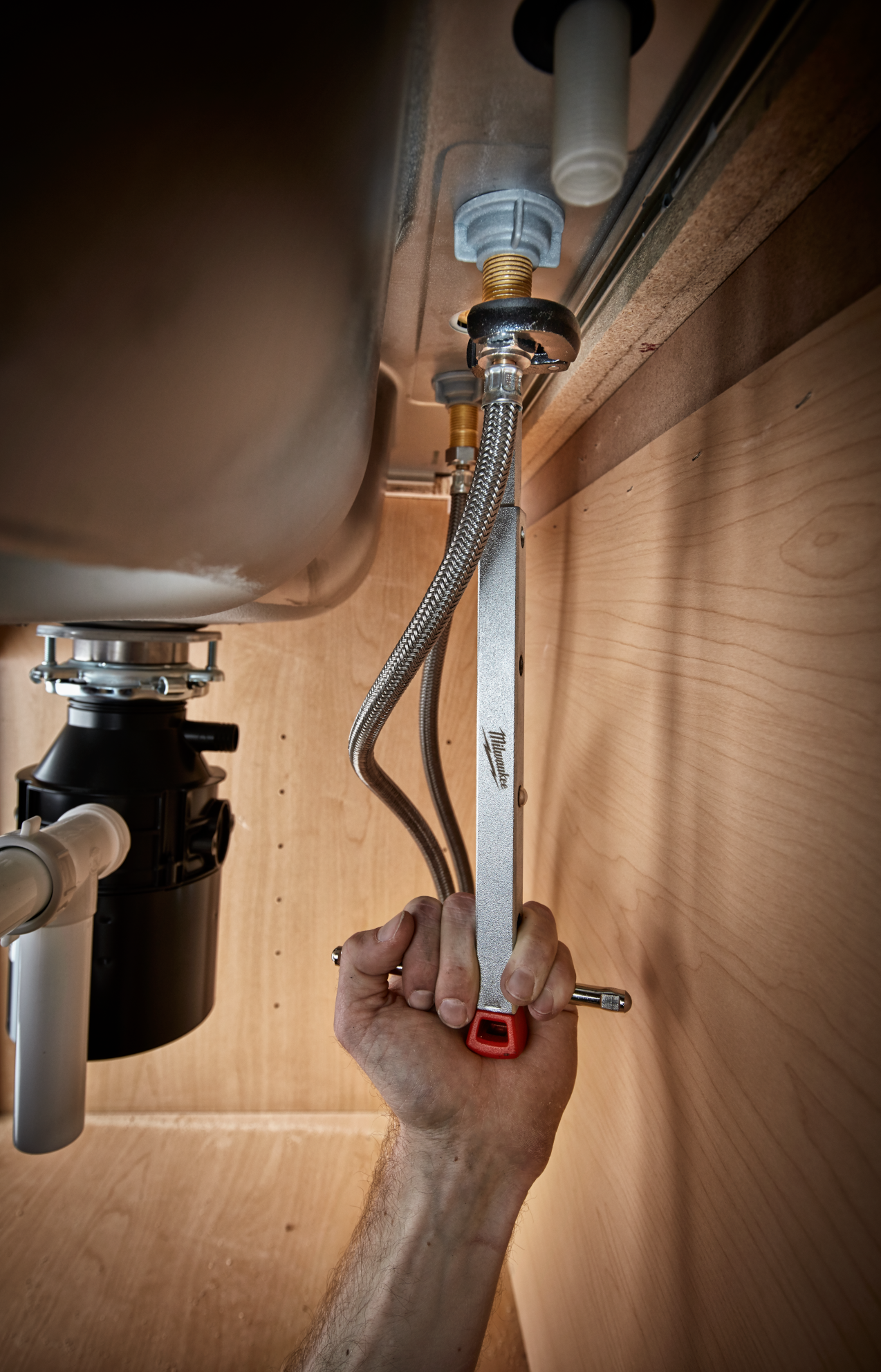 Hand using Milwaukee basin wrench on plumbing fittings under kitchen sink for home improvement tasks