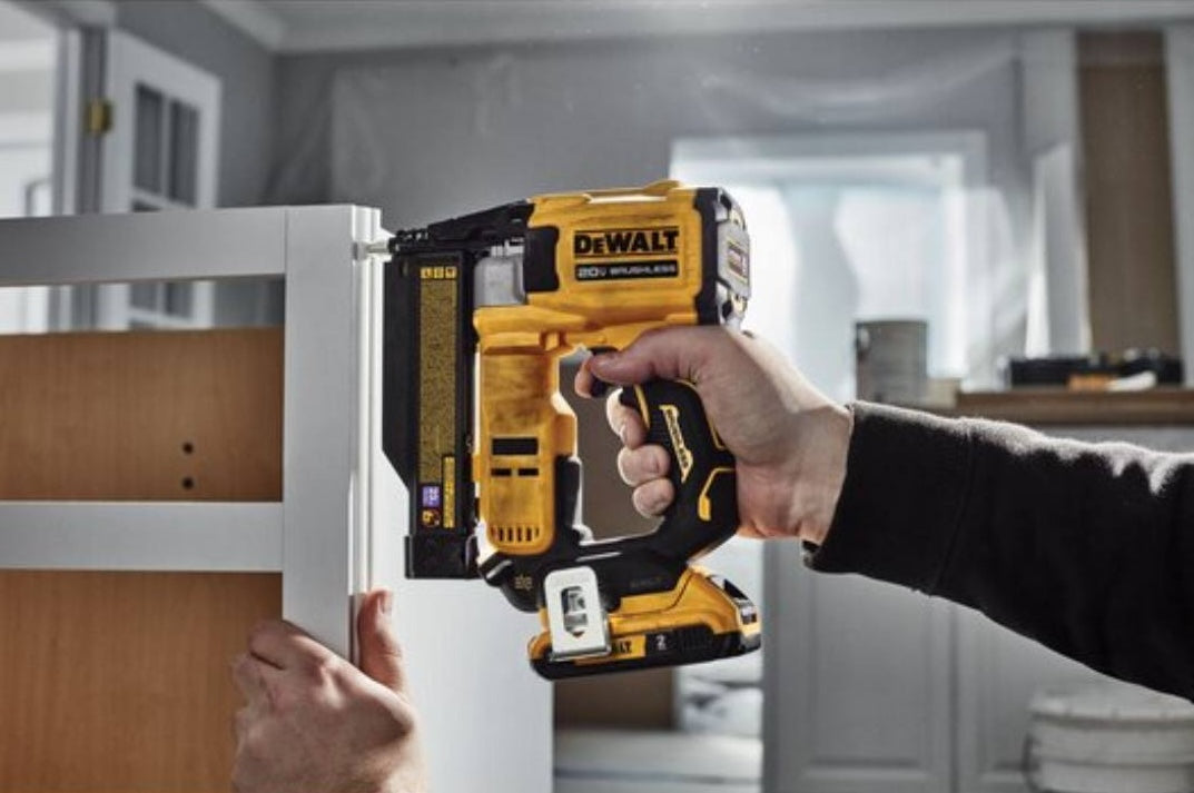 Yellow and black cordless brushless pin nailer being used for precise woodworking during home improvement tasks