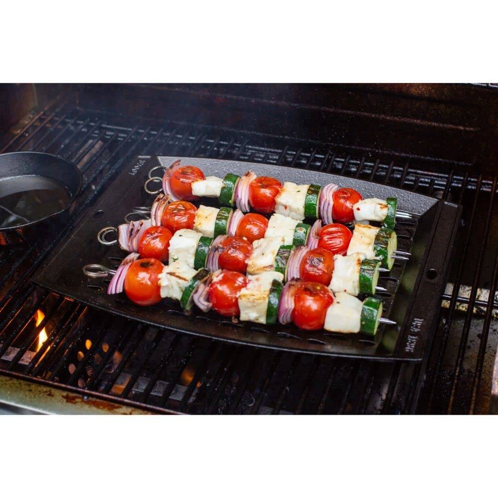 Seasoned cast iron grill topper with vegetable and cheese skewers cooking over heat on barbecue grill grate
