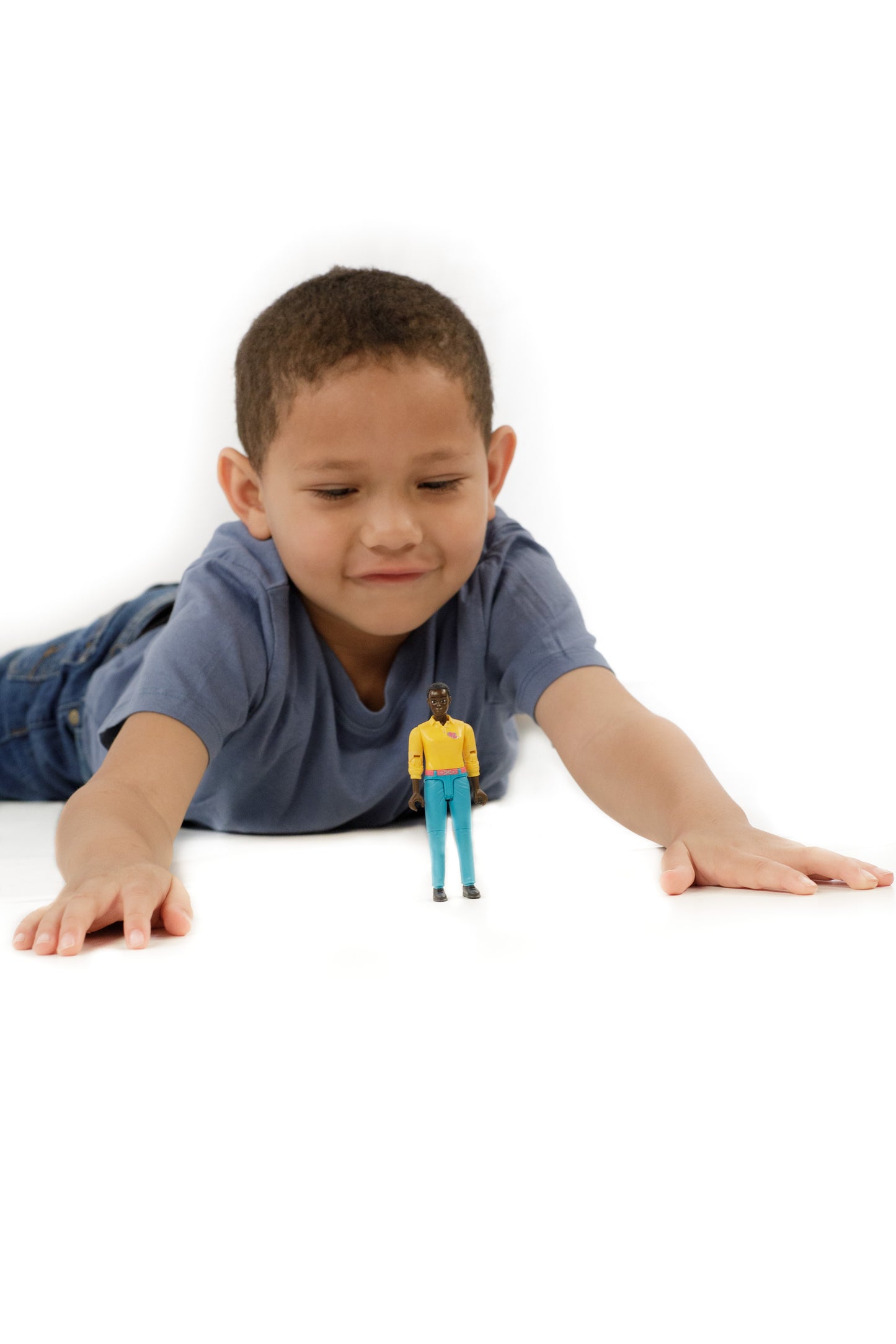 Child lying down reaching toward dark skin woman action figure in yellow top and turquoise jeans from Toys & Games collection