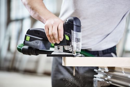 Handheld cordless barrel grip jigsaw cutting a wooden board in workshop for home improvement tools collection