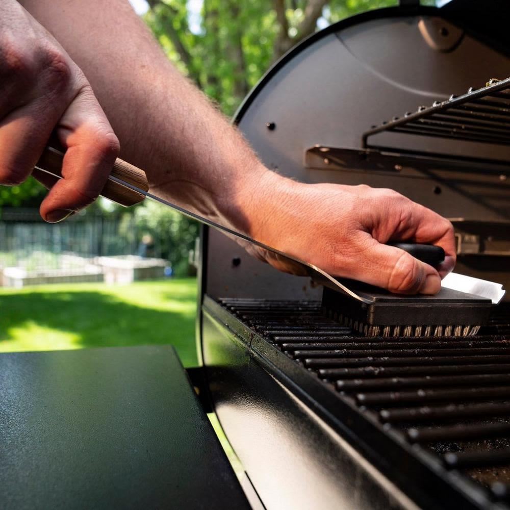 Hand using grill cleaning brush with nylon bristles on outdoor grill grate for grilling accessories and maintenance