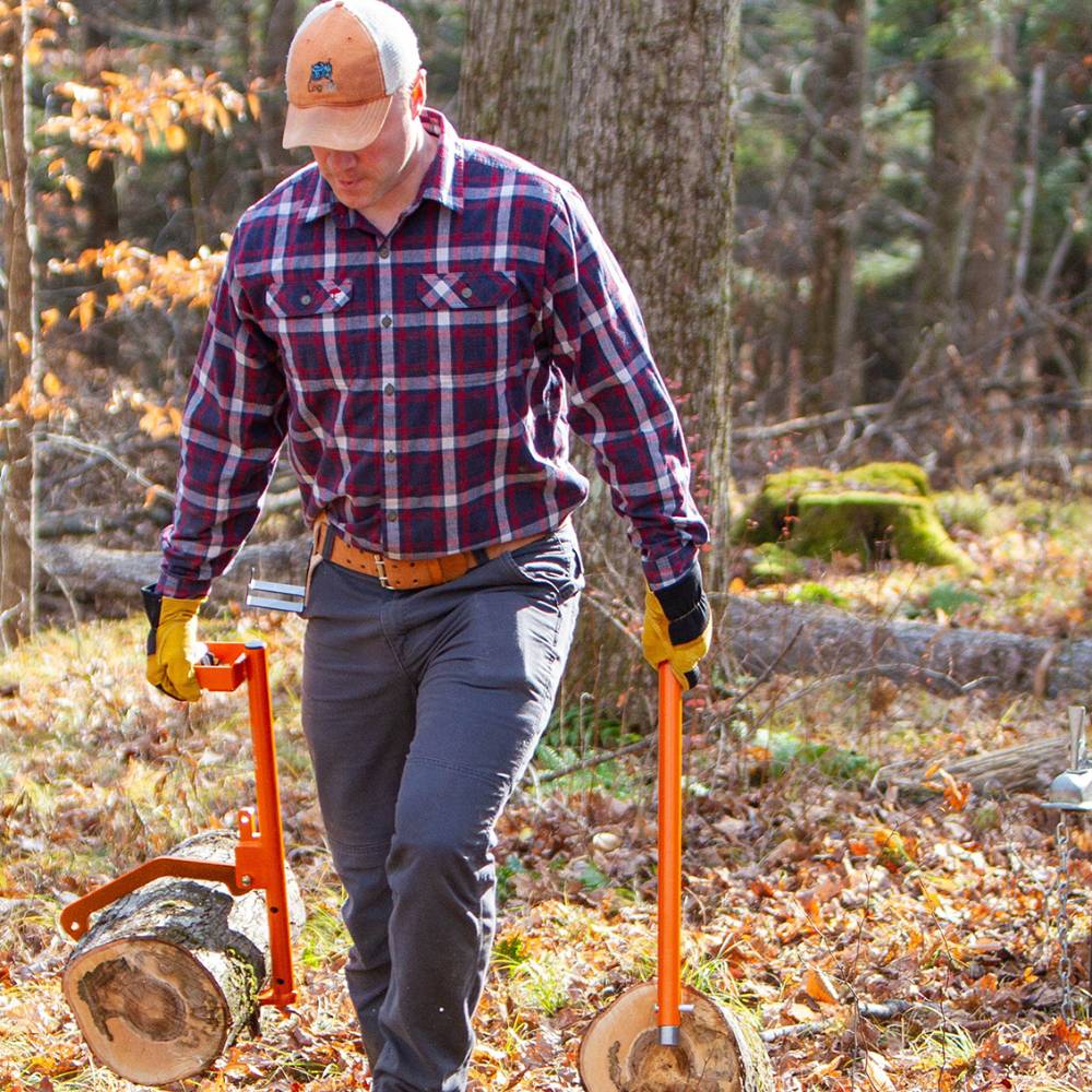 Man wearing gloves and plaid shirt using orange log handling tools to carry logs in a wooded area