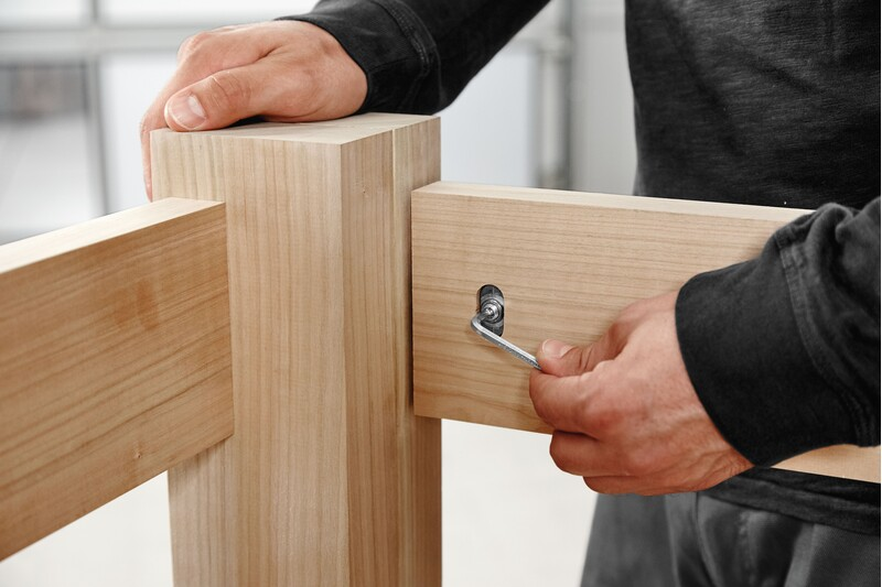 Hand securing wooden joint with metal cross anchor and Allen wrench in woodworking tool accessories for home improvement projects