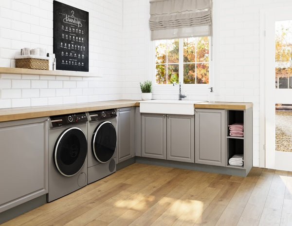 Laundry room with compact front load washers in pearl steel integrated below wooden countertop and gray cabinets