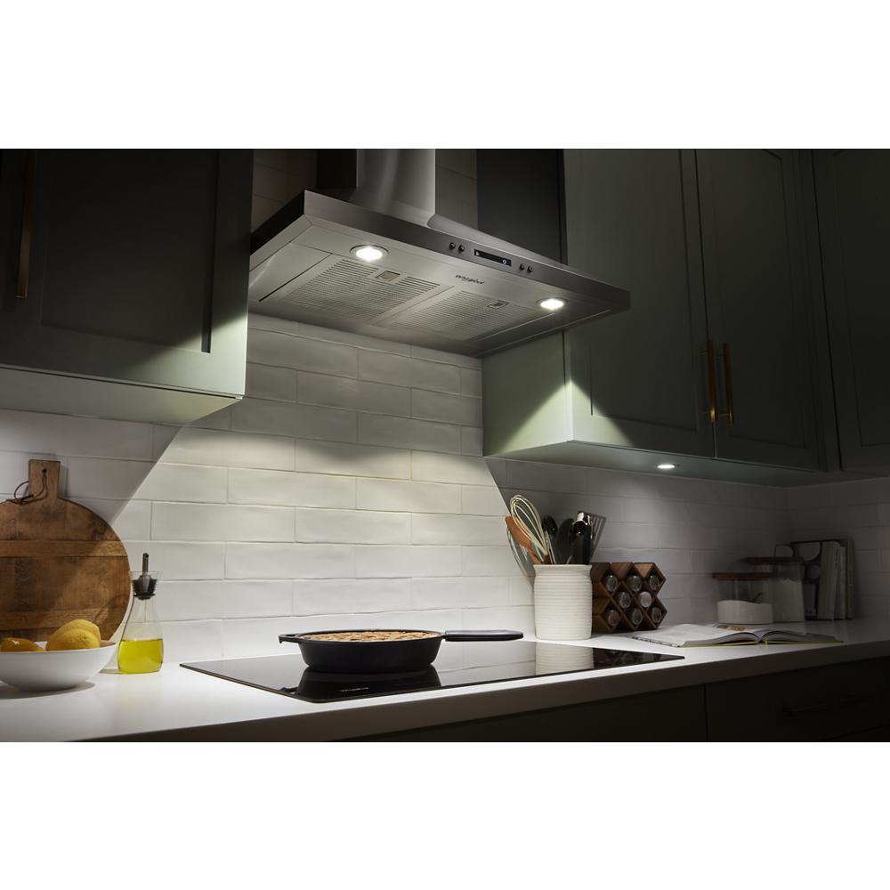Illuminated stainless steel chimney range hood above electric stove in modern kitchen with gray cabinetry and white backsplash