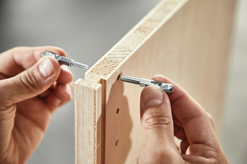 Hands installing metal panel connectors into wood panels for stable knock-down joinery in woodworking tool accessories collection