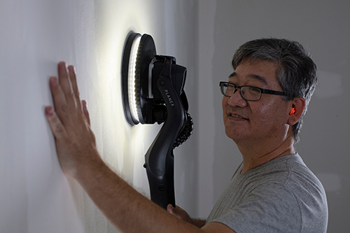Man wearing ear protection using drywall sander with built-in light for home improvement wall smoothing tasks