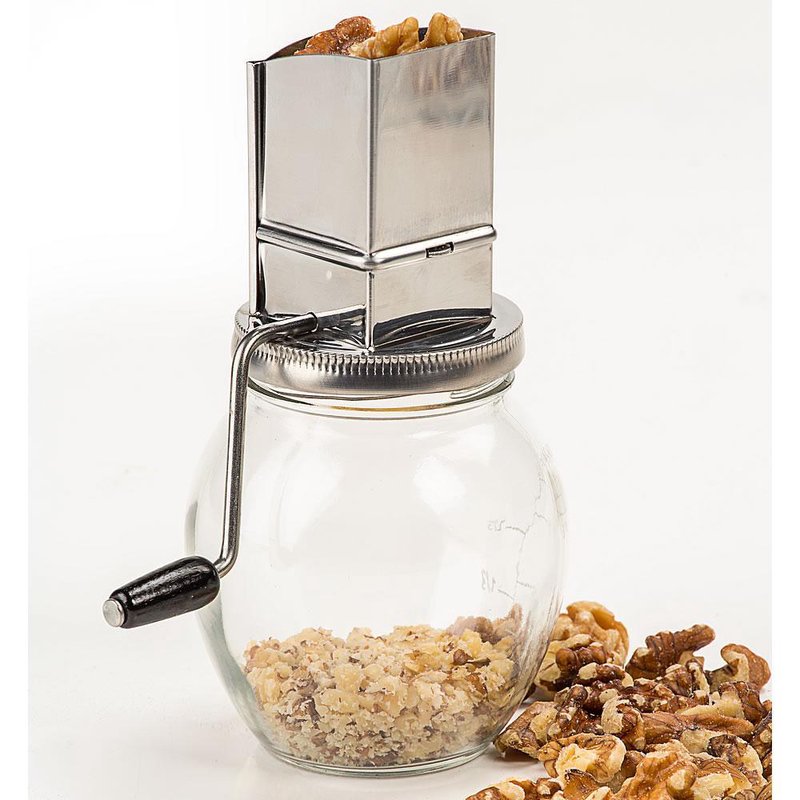 Clear glass jar nut grinder with metal crank handle and stainless steel hopper filled with walnut pieces