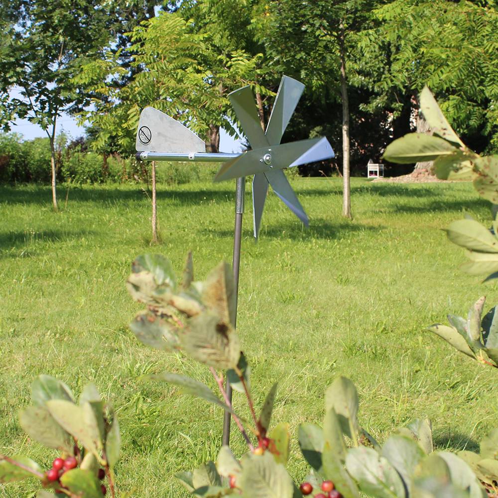 Spinning metal garden windmill with angled blades and tail vane mounted on pole for mole pest control in lawn setting