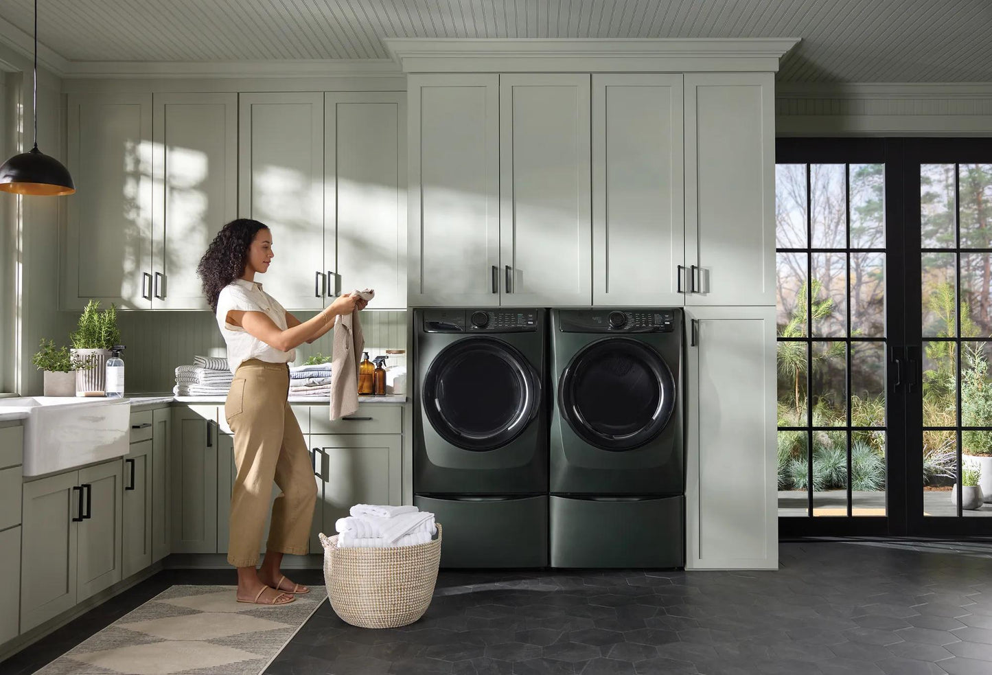 Woman examining laundry near dark gray front load gas dryer and washer in bright modern laundry room from Dryers and Appliances collections
