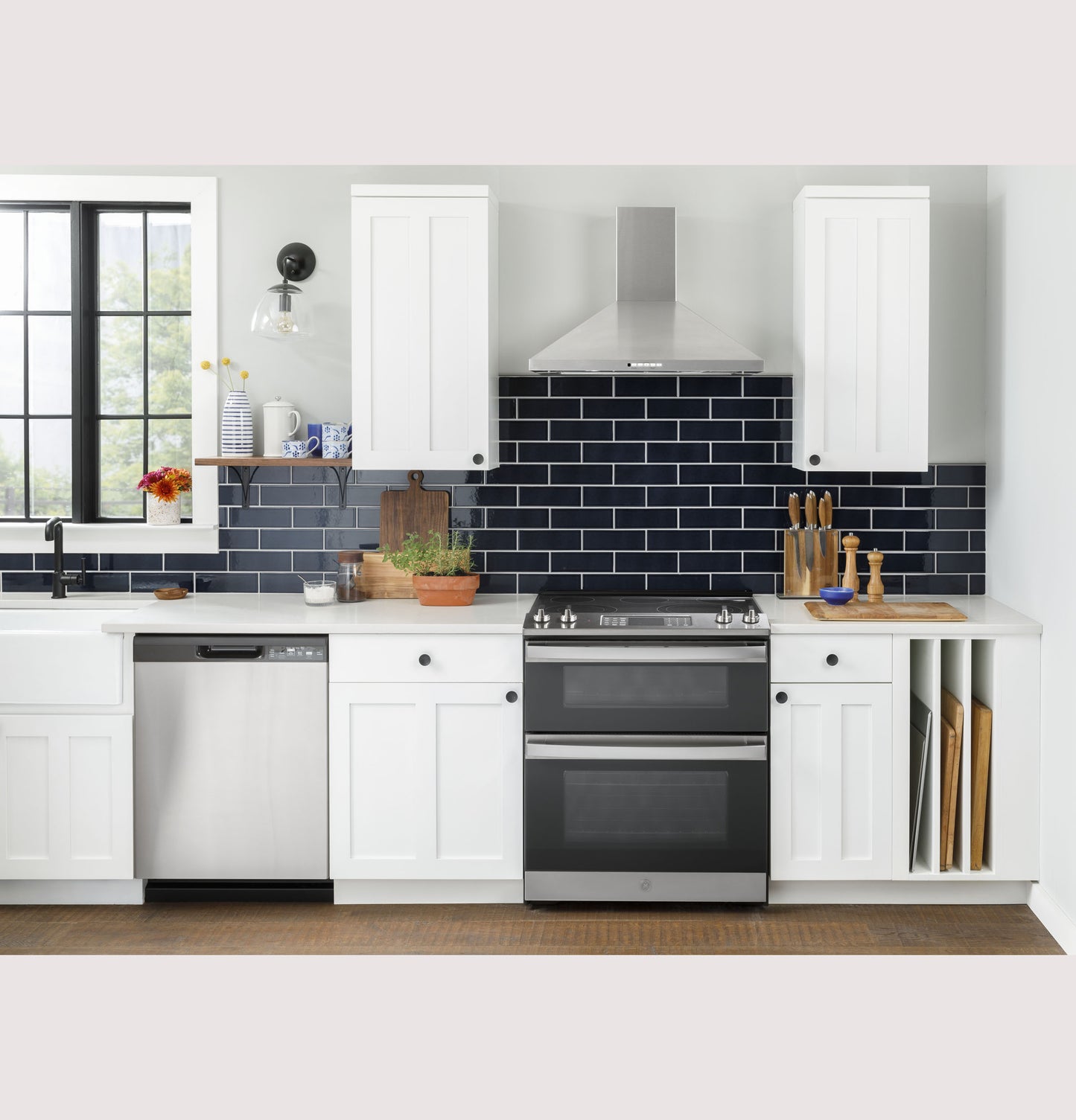 Modern kitchen scene with stainless steel slide-in electric convection double oven range, white cabinetry, and dark tile backsplash