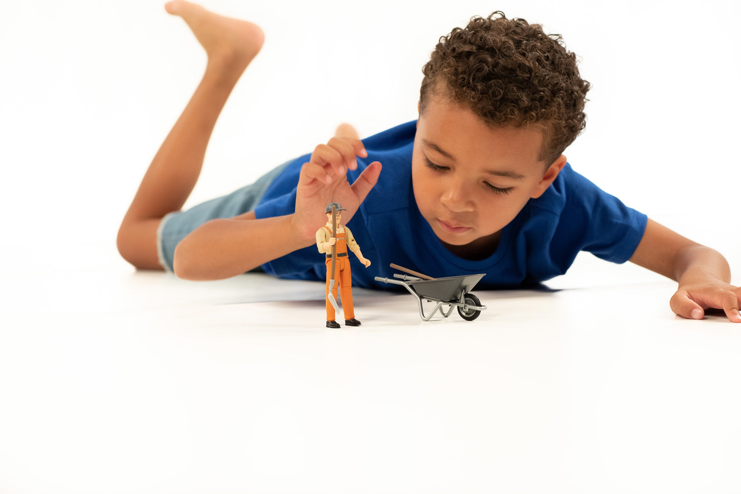 Young boy in blue shirt playing with miniature worker figure and gray wheelbarrow for home improvement playset