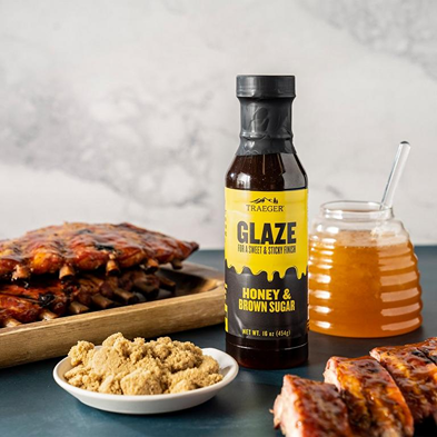 Bottle of Traeger honey and brown sugar glaze with ribs, jar of honey, and brown sugar bowl in grilling sauces and spices collection
