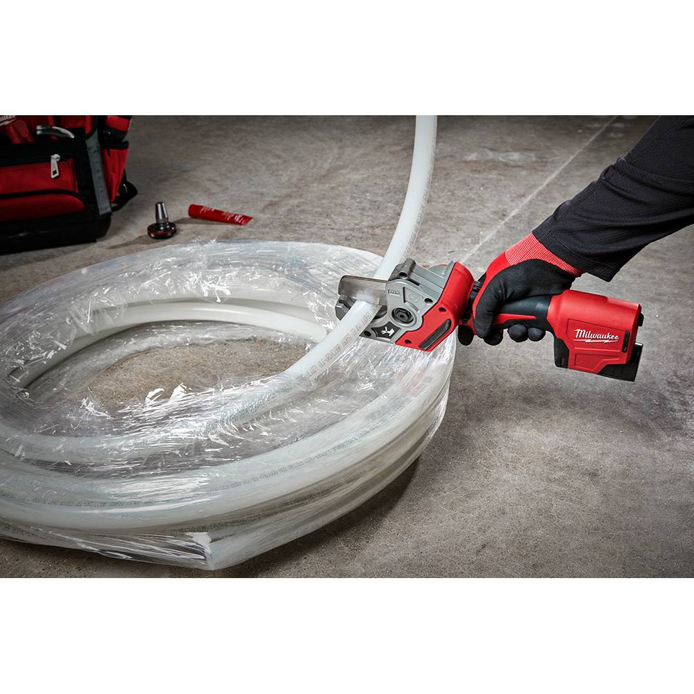 Red and black cordless Milwaukee pipe shear cutting through white plastic tubing on concrete surface for home improvement use