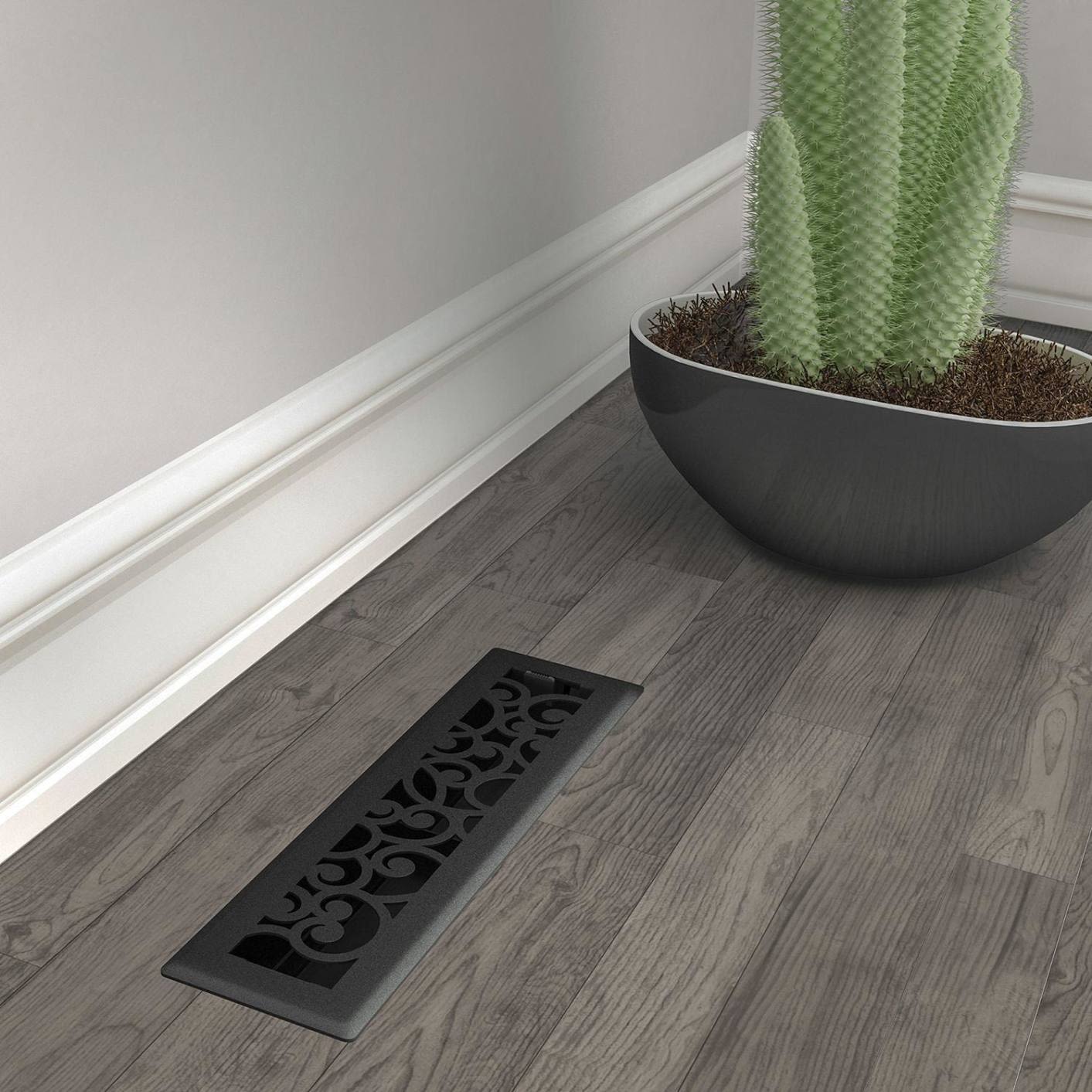 Black iron floor register with ornamental scrollwork on dark wood floor for home improvement and plumbing ventilation