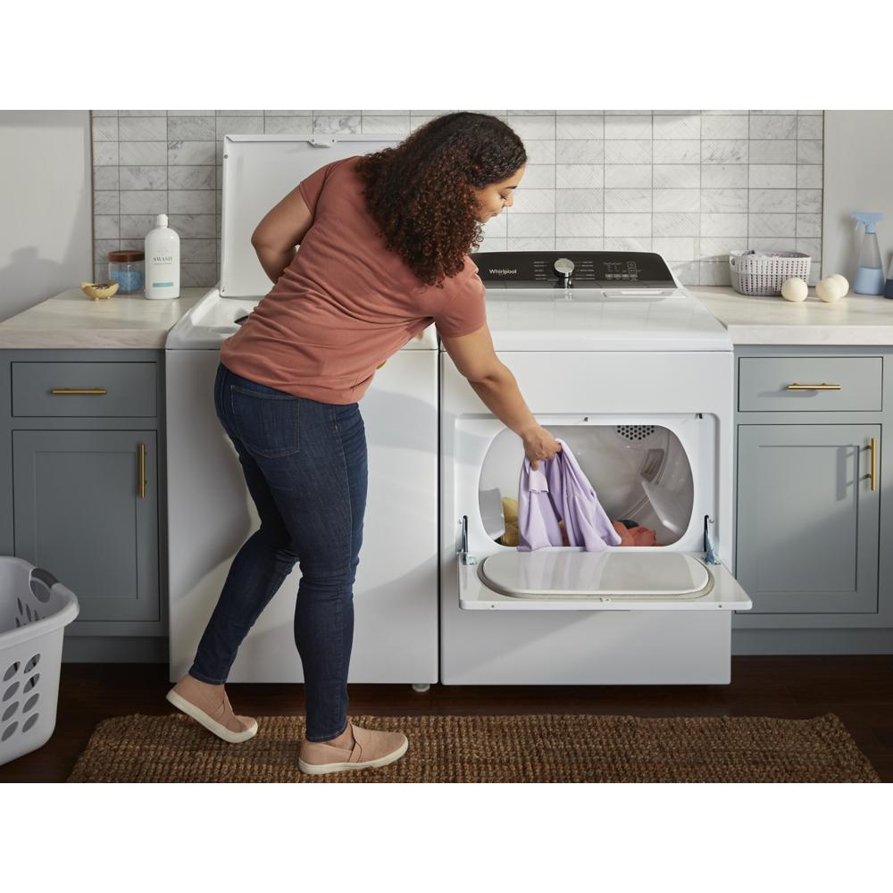 Woman removing clothes from white top load gas dryer in modern laundry room with gray cabinets and gold hardware