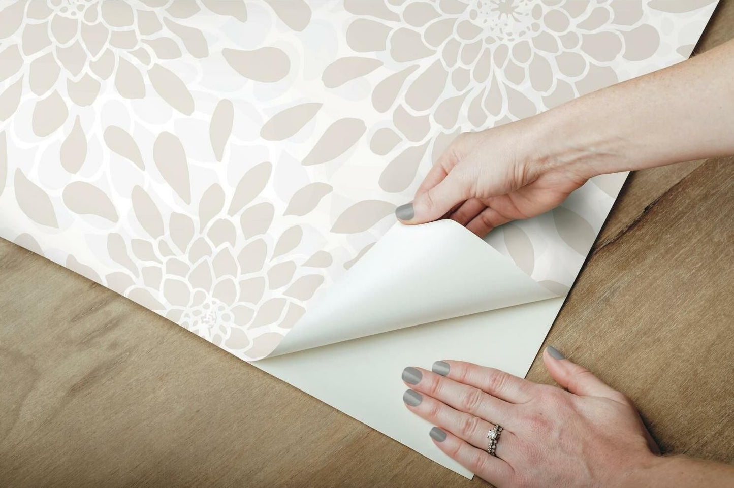 Hands applying neutral floral peel and stick wallpaper on wooden surface for easy room update