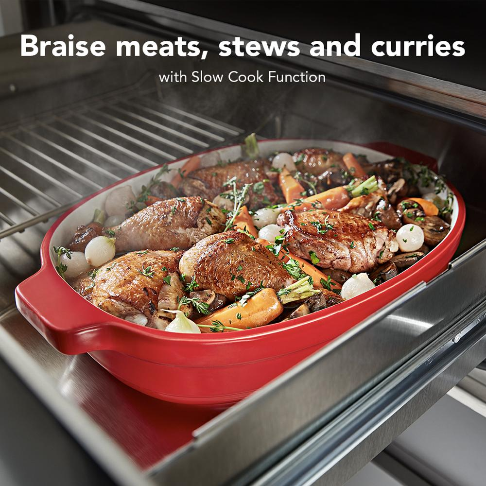 Red ceramic dish with slow-cooked chicken, carrots, onions, and herbs inside a warming drawer in KitchenAid appliances collection