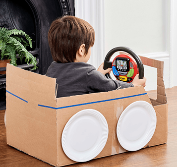 Child using interactive steering wheel toy in cardboard car with paper plate wheels in pretend play toys collection