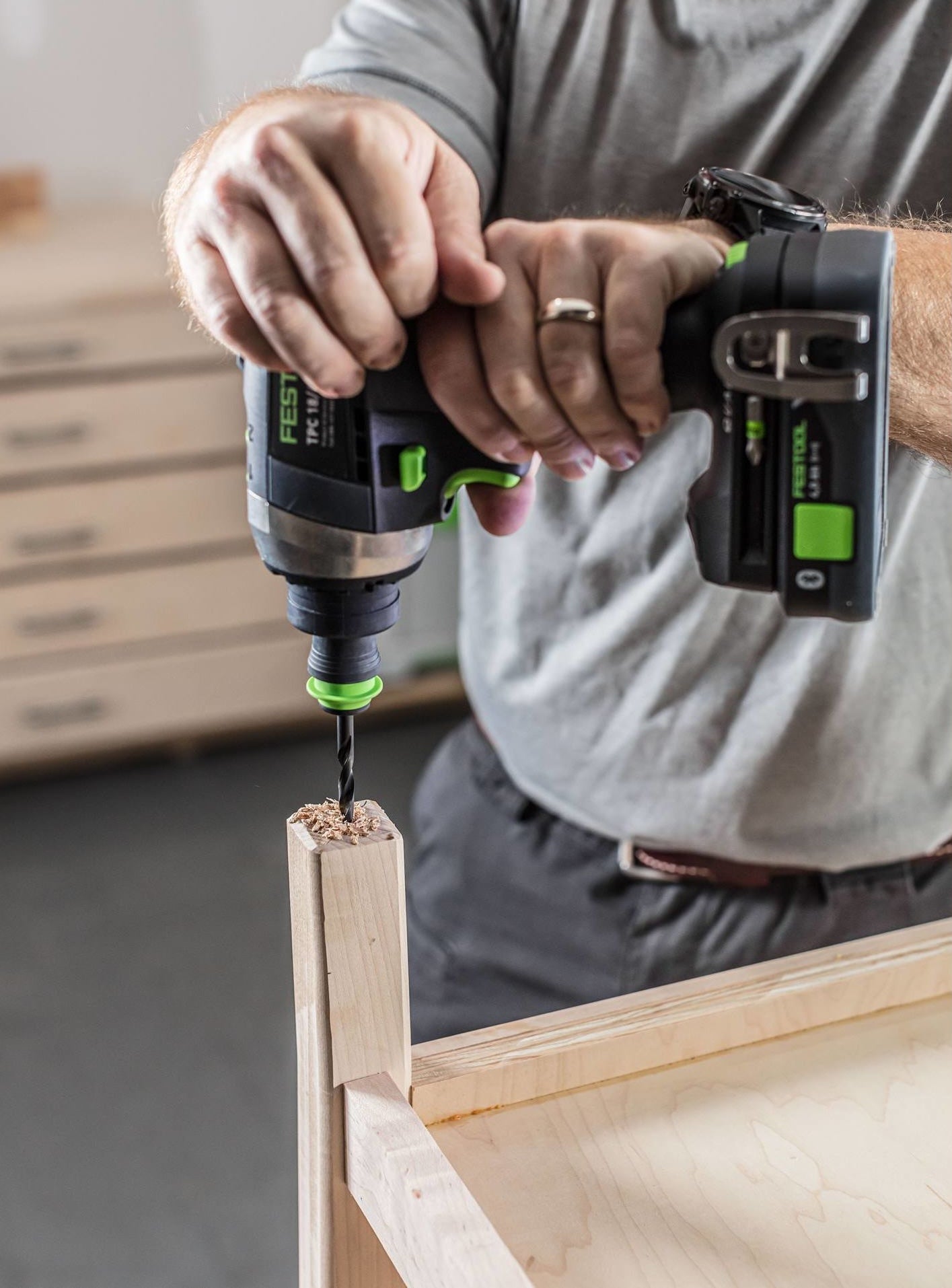 Man using Festool cordless drill with brad point bit to drill into wooden furniture in workshop setting