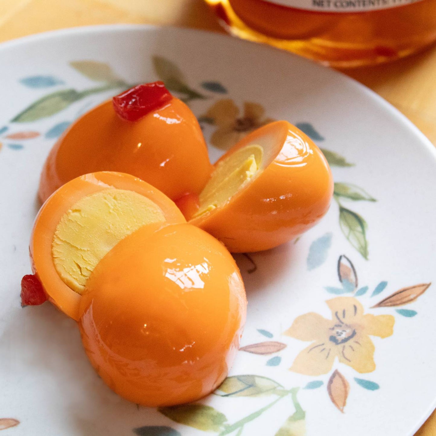 Hard-boiled eggs coated in spicy orange brine with red chili pieces on a floral plate for food and beverage collection