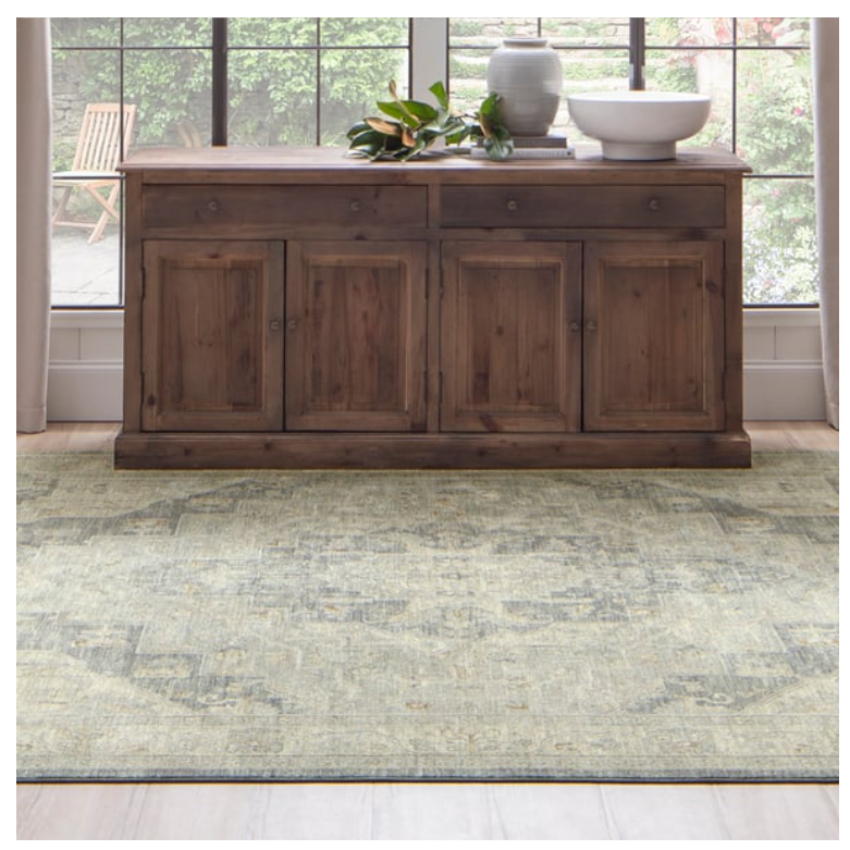 Light-toned rug with subtle geometric patterns placed beneath a dark wooden sideboard in a bright room setting