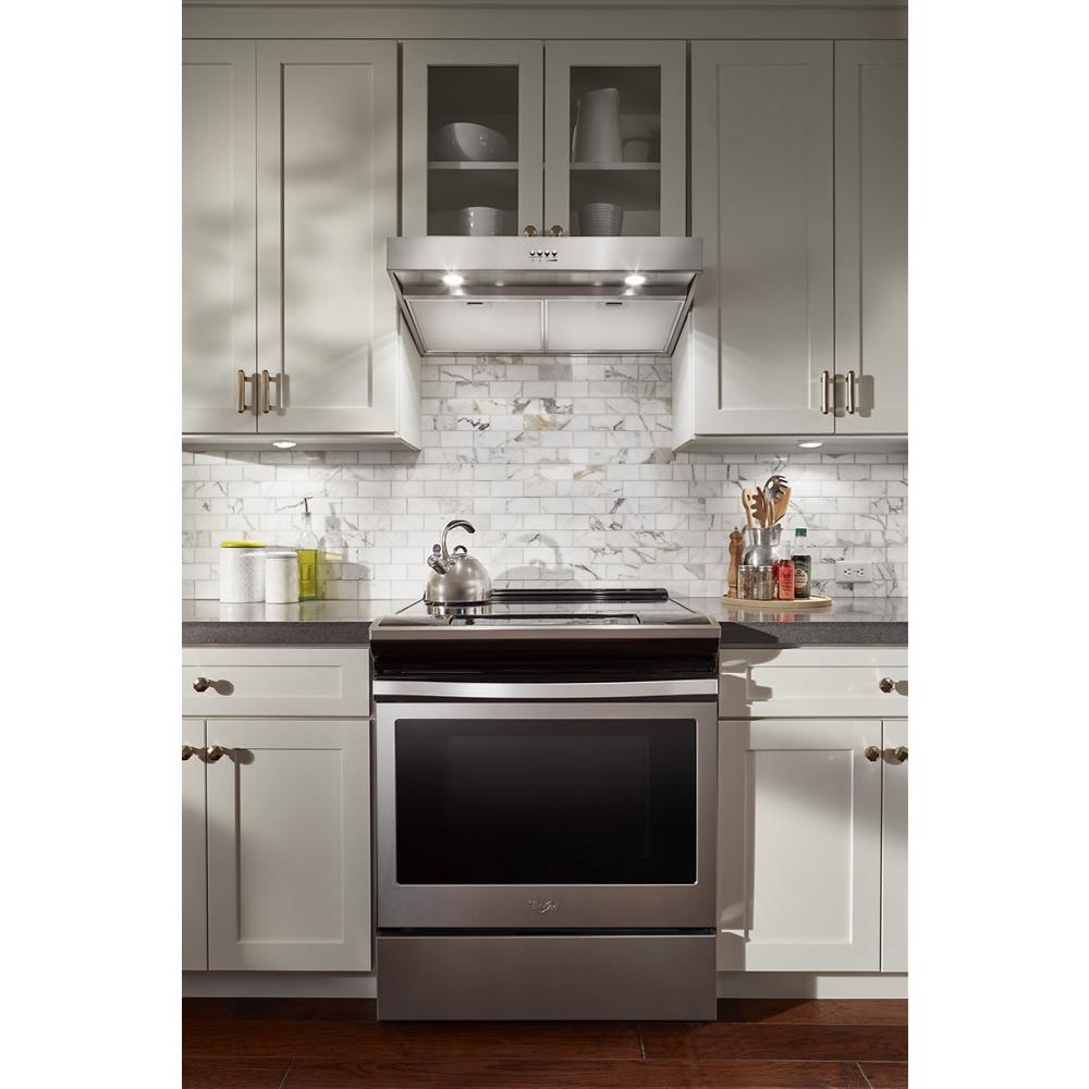 Stainless steel kitchen range hood with LED lighting installed above stove in modern kitchen with white cabinetry.