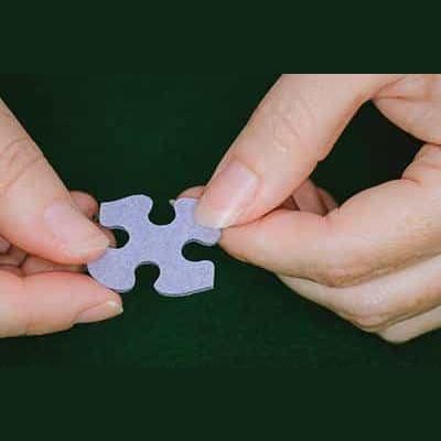 Two hands holding a single light purple puzzle piece for Toys & Games and Puzzles under $50 collection.