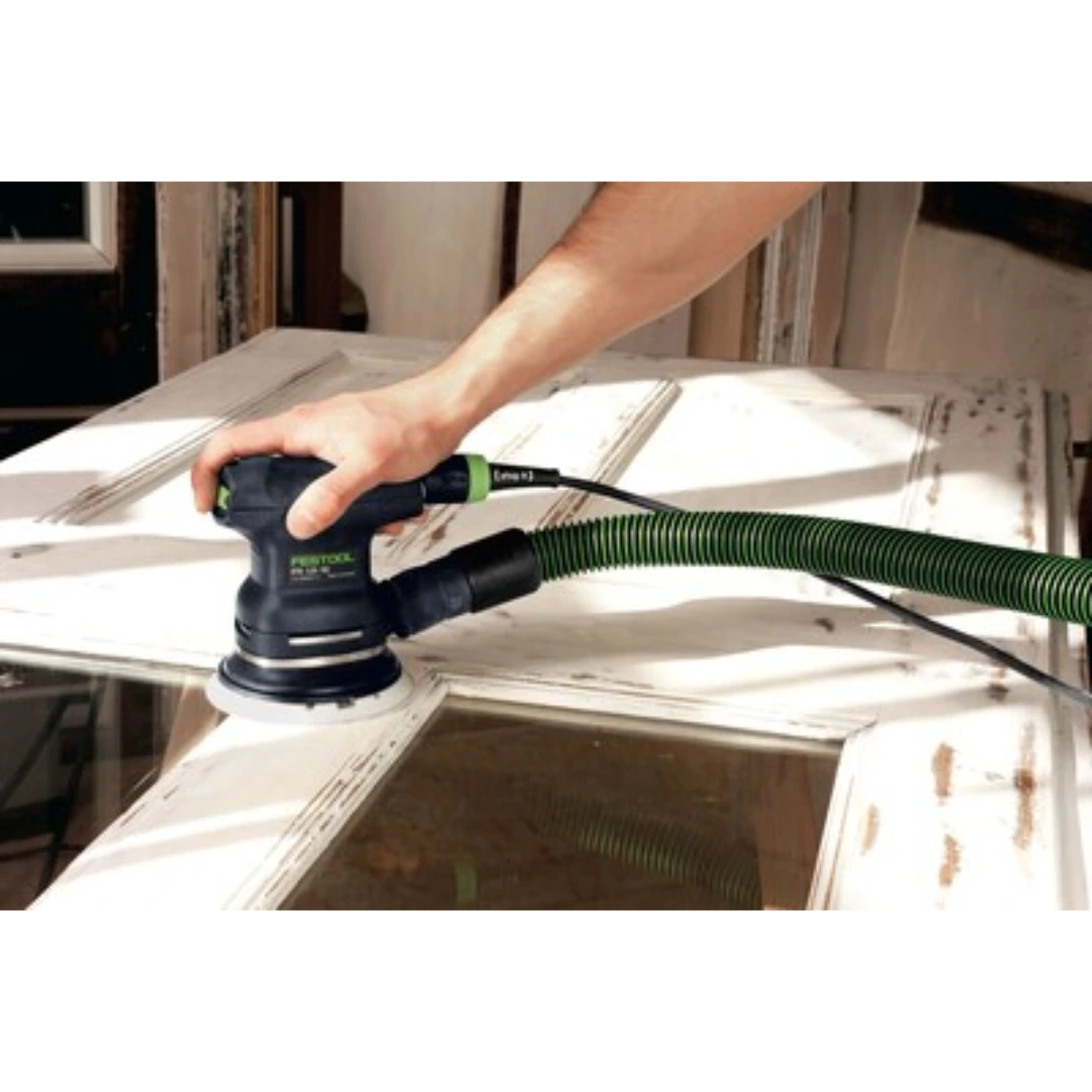 Hand operating a Festool sander with green vacuum hose on a distressed white wooden door for home improvement.