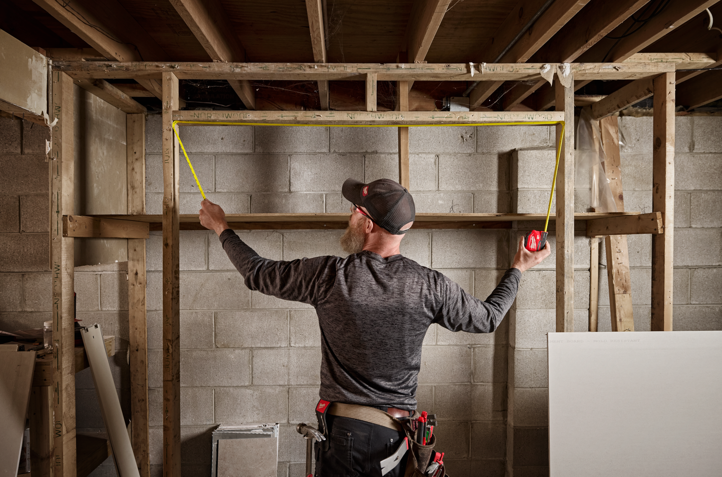 Man measuring wooden frame with a Milwaukee compact auto-lock tape measure for woodworking and home improvement tasks