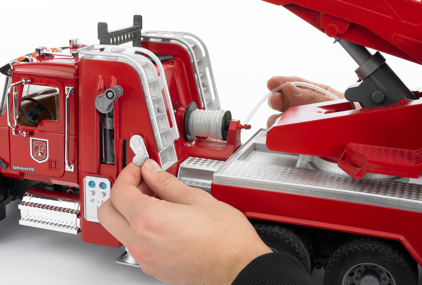 Hands operating controls on red Bruder Toys fire engine model with detailed ladder and water pump features
