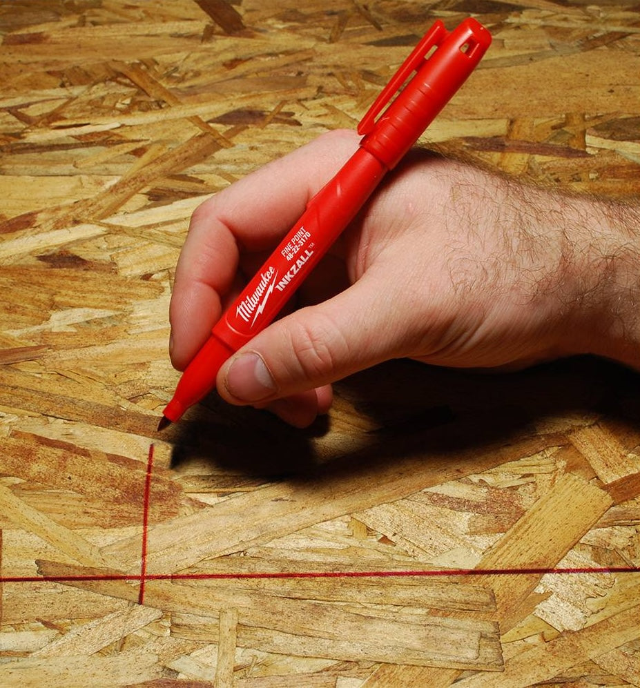 Hand marking on rough OSB wood surface with red jobsite marker from Milwaukee hand tools collection
