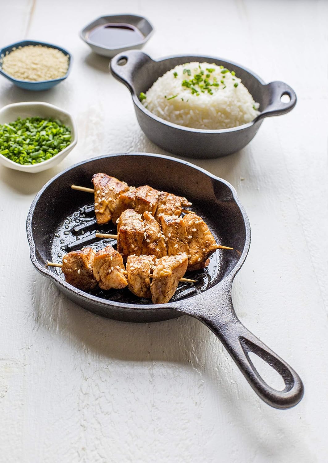 Small cast iron grill pan with kabobs cooking, accompanied by rice and seasonings in stoneware bowls for kitchenware use