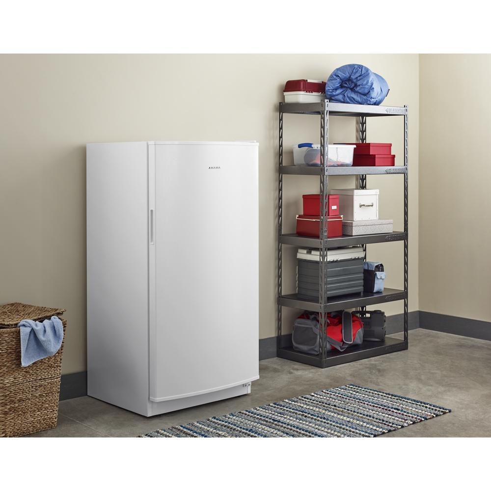 White upright freezer with energy-saving insulation in a storage room with metal shelving and woven basket nearby