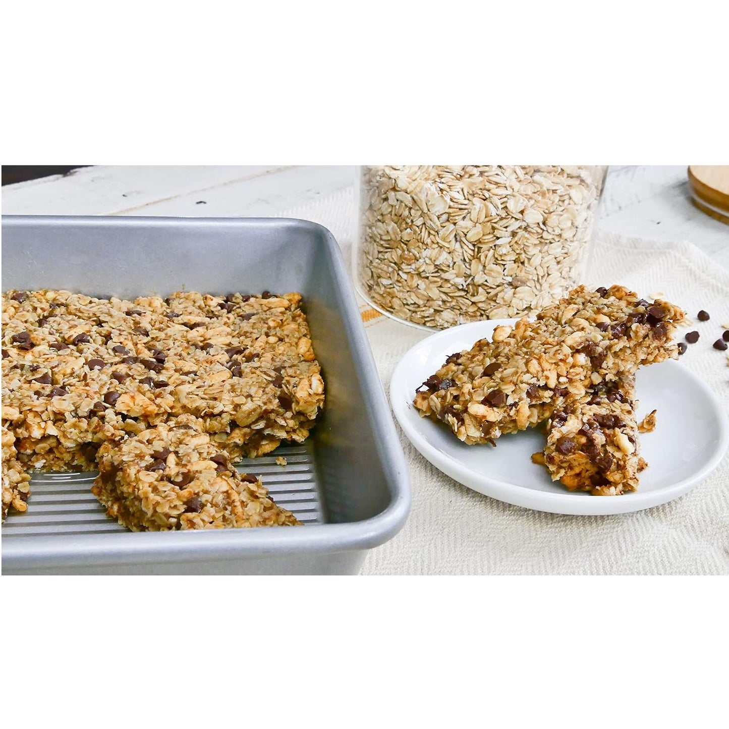 Square metal cake pan with homemade oatmeal chocolate chip bars, shown with ingredients in kitchenware collections