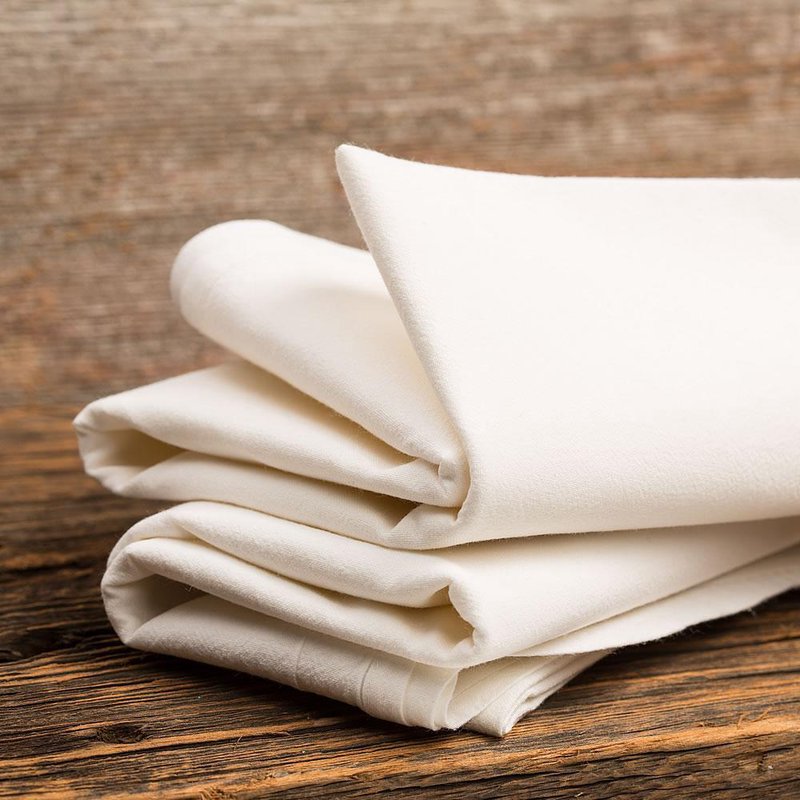 Stack of soft natural cotton flour sack towels folded on rustic wooden surface in kitchenware collection under fifty dollars