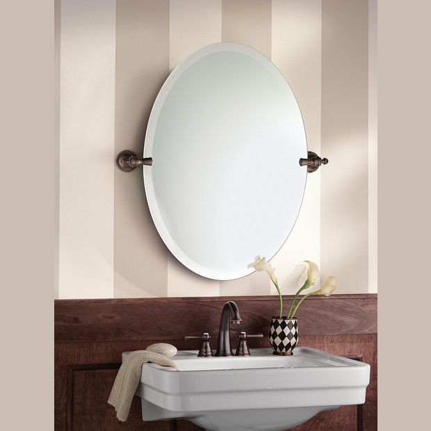 Oval wall mirror with oil rubbed bronze frame mounted above bathroom sink and decorative vase with flowers