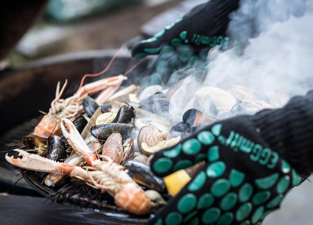 Hands wearing heat-resistant grilling gloves handling shellfish on a smoky outdoor grill in outdoor living collections