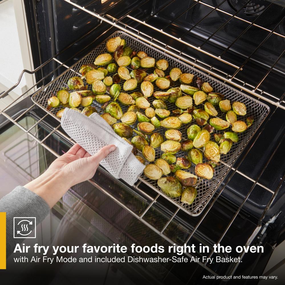 Hand removing air fry basket with roasted Brussels sprouts from oven in kitchen appliances and home improvement collection