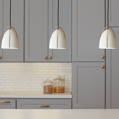 Three white matte dome pendant lights with satin brass accents hanging over kitchen countertop with gray cabinetry