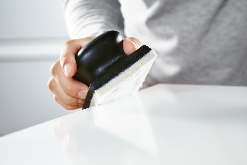 Handheld black polishing tool with white felt pad used for smoothing surfaces in tools and home improvement tasks