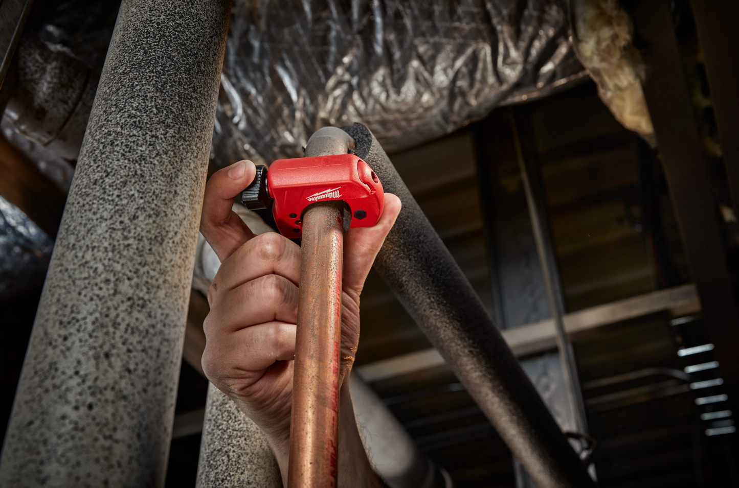 Hand gripping red Milwaukee mini tubing cutter trimming copper pipe during home improvement plumbing work