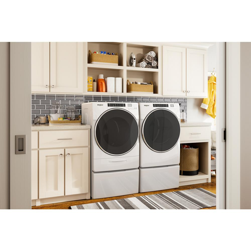 White front load washer and gas dryer set with pedestal drawers under beige cabinets in a modern laundry room