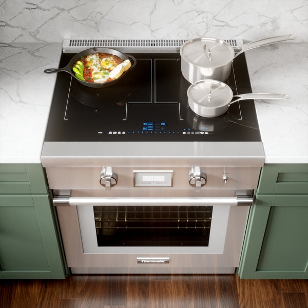 Stainless steel induction cooktop and oven with digital controls, showing cookware and marble countertop in kitchen setting