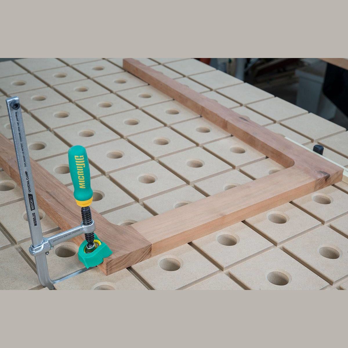 Green and silver Microjig clamp securing a wooden frame on a perforated workbench for woodworking tasks