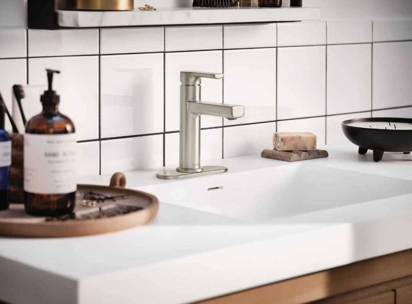 Brushed nickel single-handle bathroom faucet installed on white countertop with tiled backsplash in modern bath setting