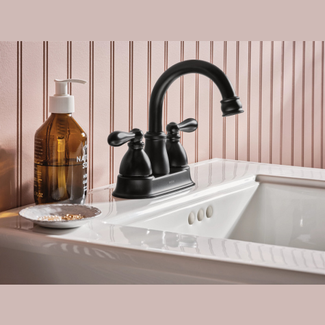 Matte black two-handle high arc faucet installed on white bathroom sink with soap dispenser nearby for home improvement