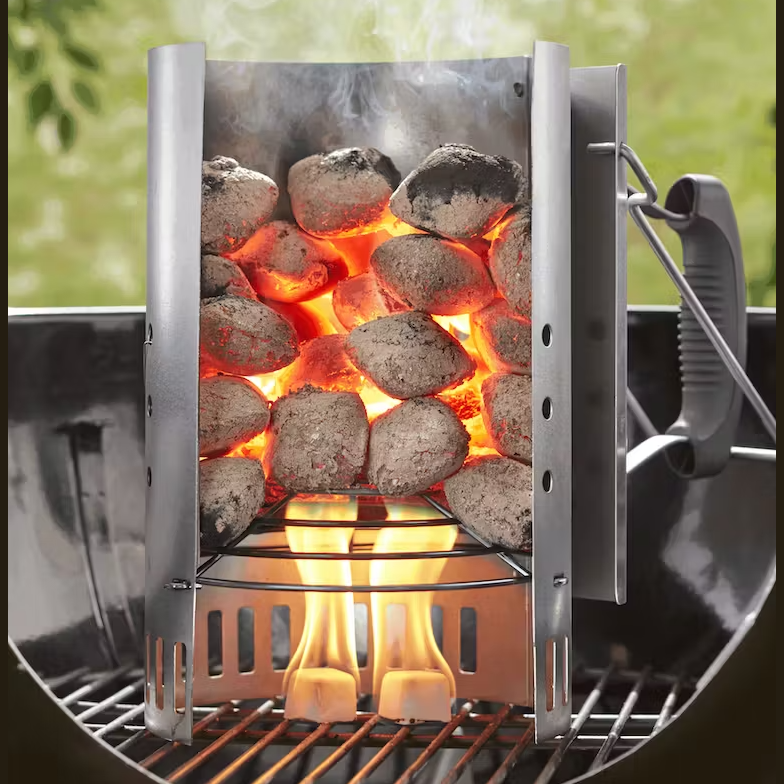 Charcoal briquettes glowing red inside a metal chimney starter with odorless fire starter cubes igniting flame below