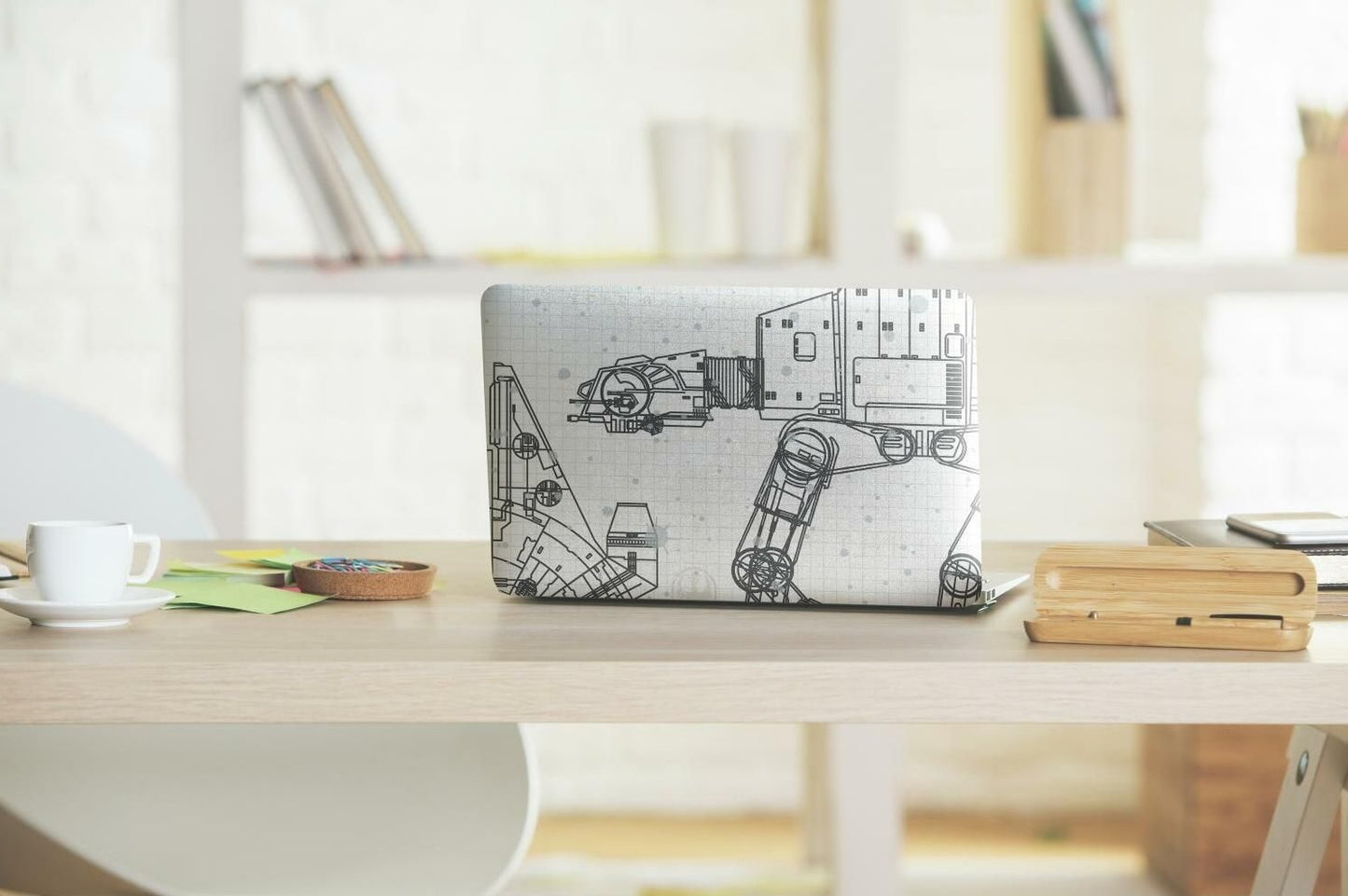 Laptop covered with peel and stick wallpaper featuring black and white Star Wars blueprint designs on a wood desk